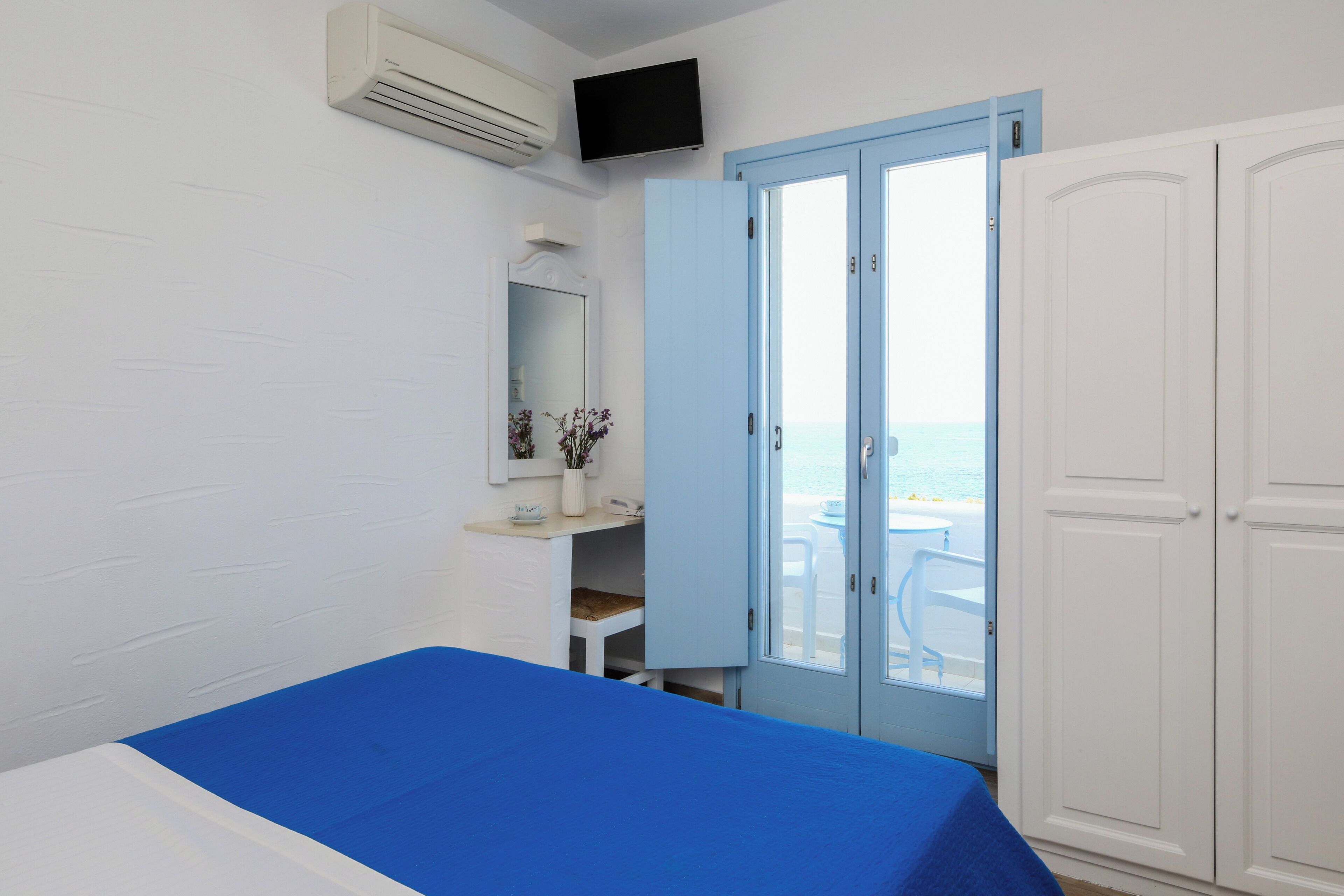A room with a bed, a wardrobe, a television, and a door leading to a balcony with a view.
