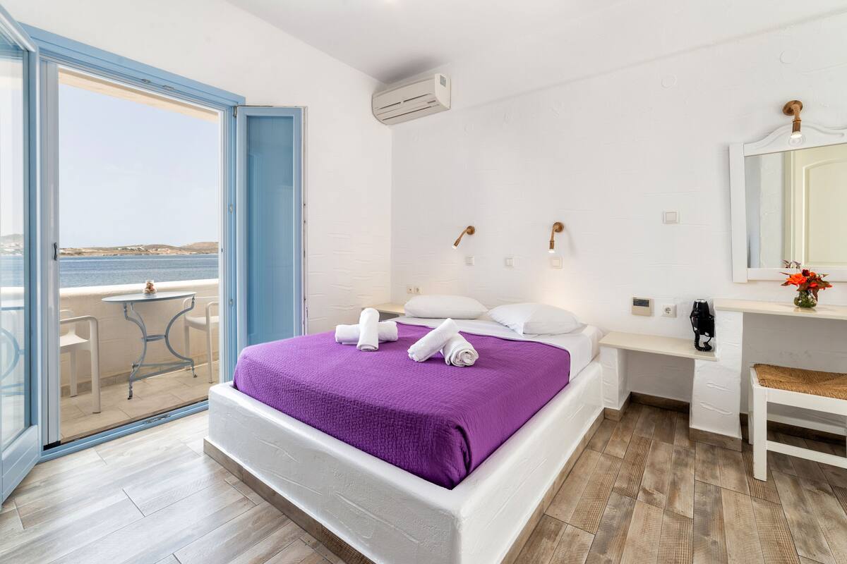 Un dormitorio con cama, mesita de noche, espejo y vista al mar a través de una puerta corrediza.