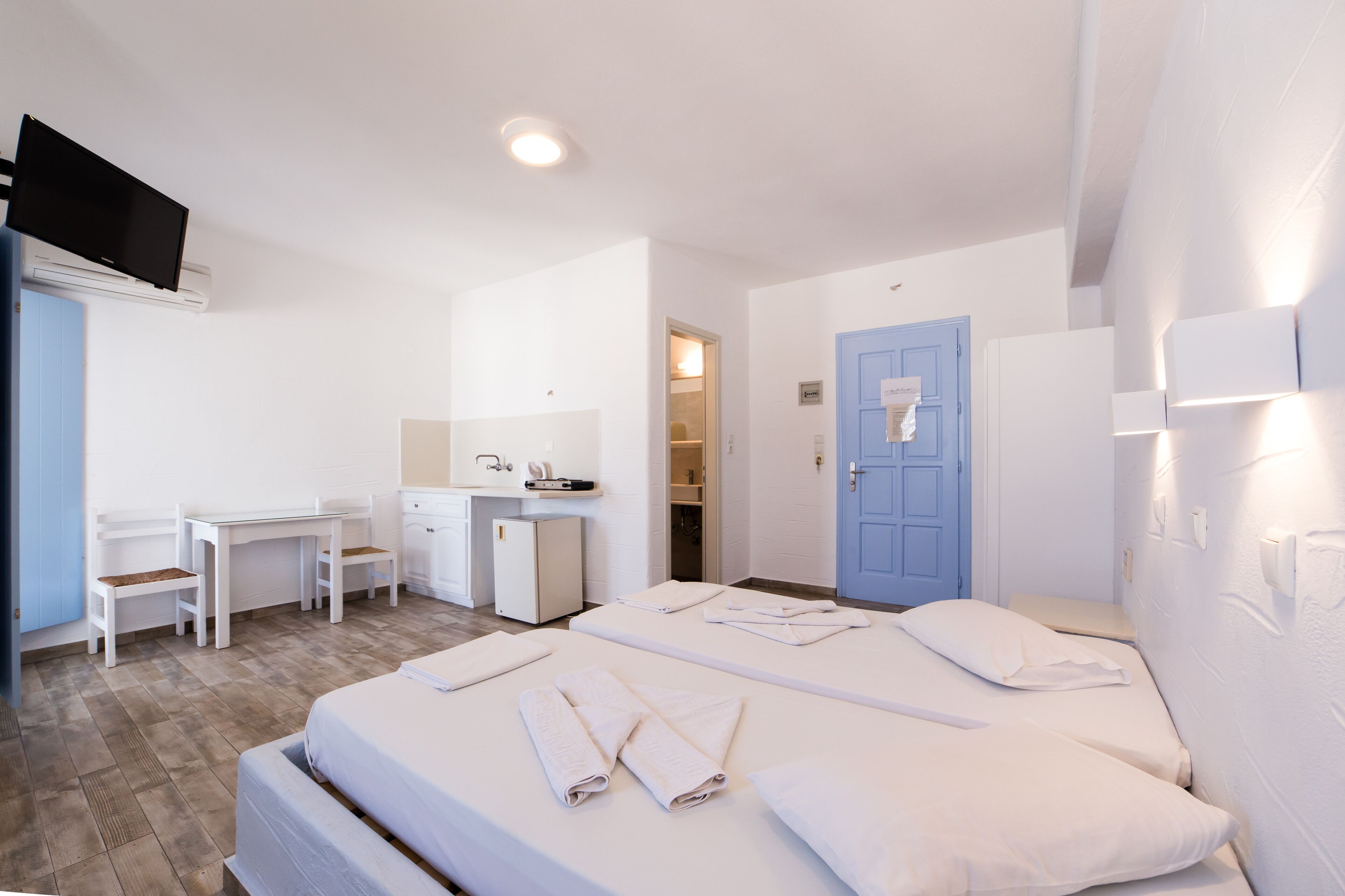A hotel room with two beds, a desk, a small kitchenette, and a bathroom.