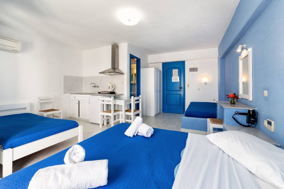 Habitación de hotel con dos camas, kitchenette, puerta azul y una pequeña zona de estar.
