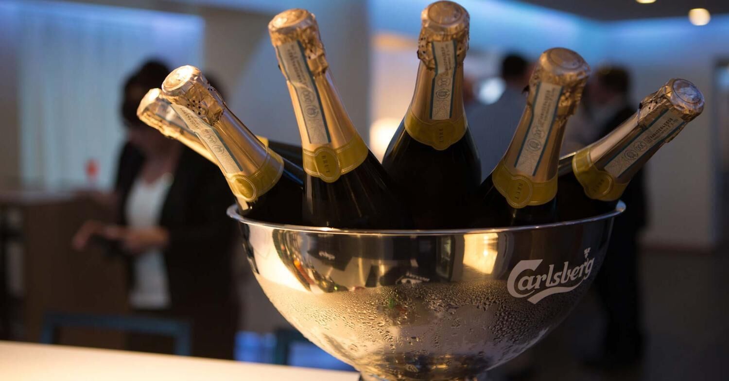 En metallskål som innehåller flera champagneflaskor med korkar, och som är märkta med texten ”Carlsberg”.
