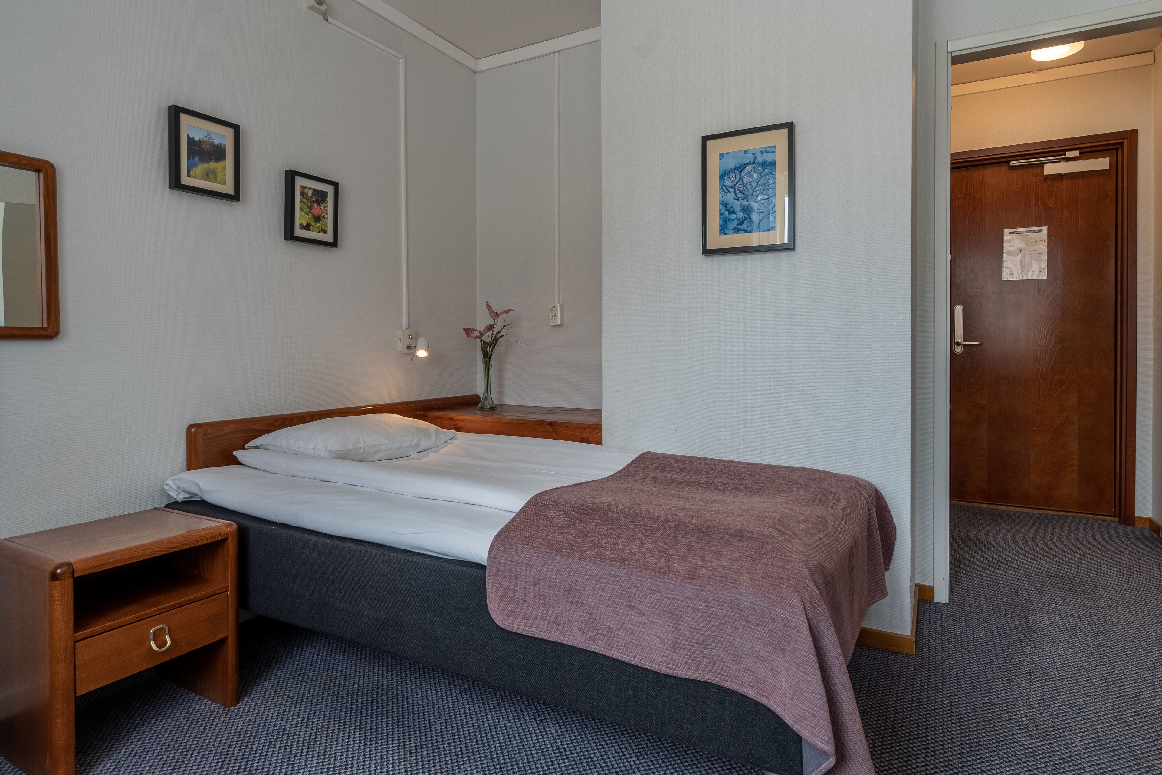 Habitació d'hotel amb un llit, una taula de nit i una porta.