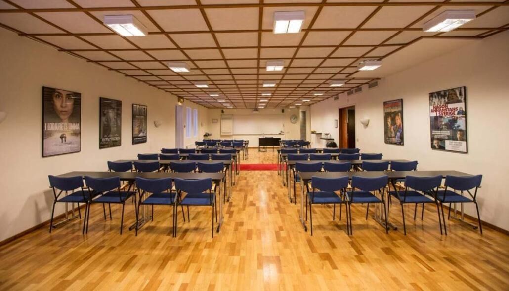 A conference room with rows of blue chairs, a wooden floor, and posters on the walls.
