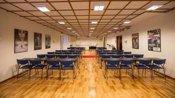 A conference room with rows of blue chairs, a wooden floor, and posters on the walls.