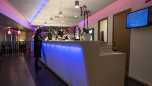 Zona de recepción de un hotel, con mostrador, televisor montado en la pared y una planta en maceta.