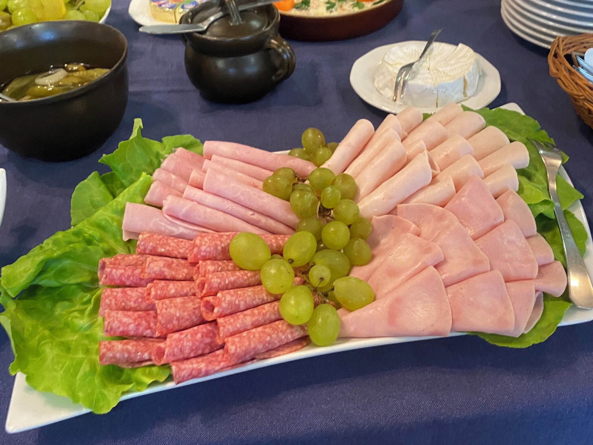 Una tabla de fiambres con diversos embutidos, queso y uvas sobre un plato blanco.