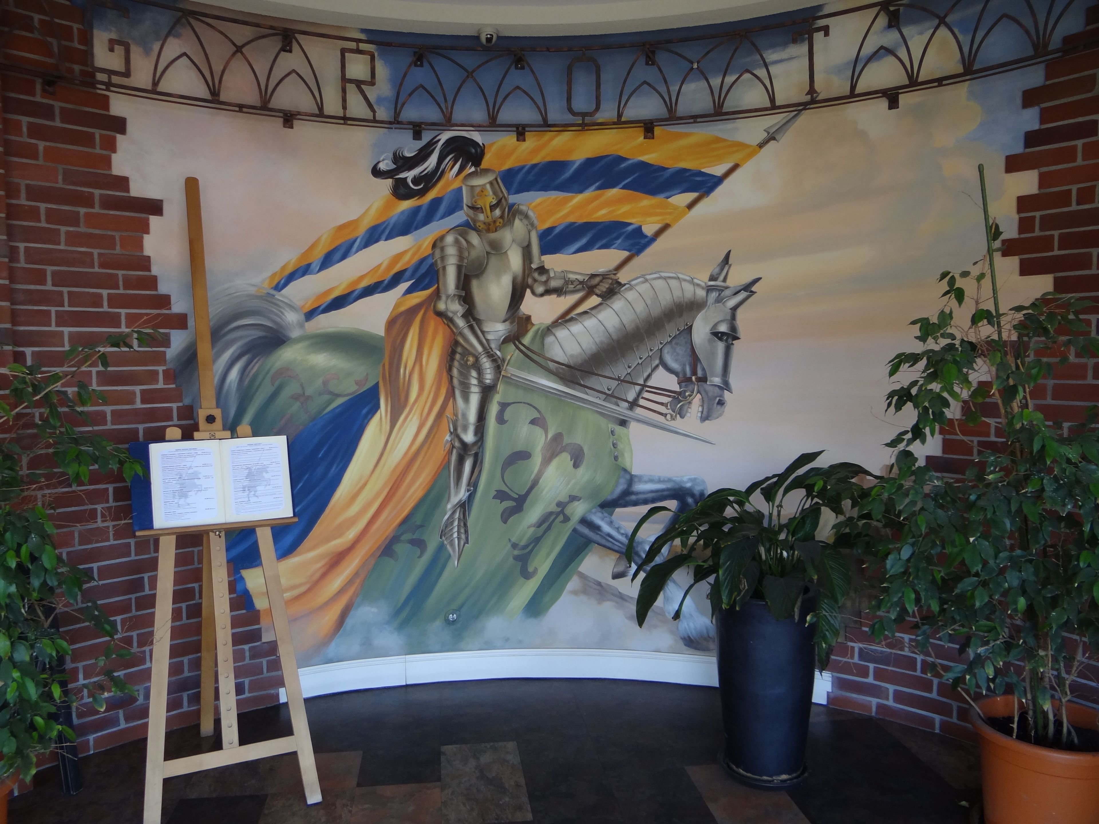 Un mural que muestra un caballero a caballo con una bandera, un caballete con un libro y macetas con plantas.