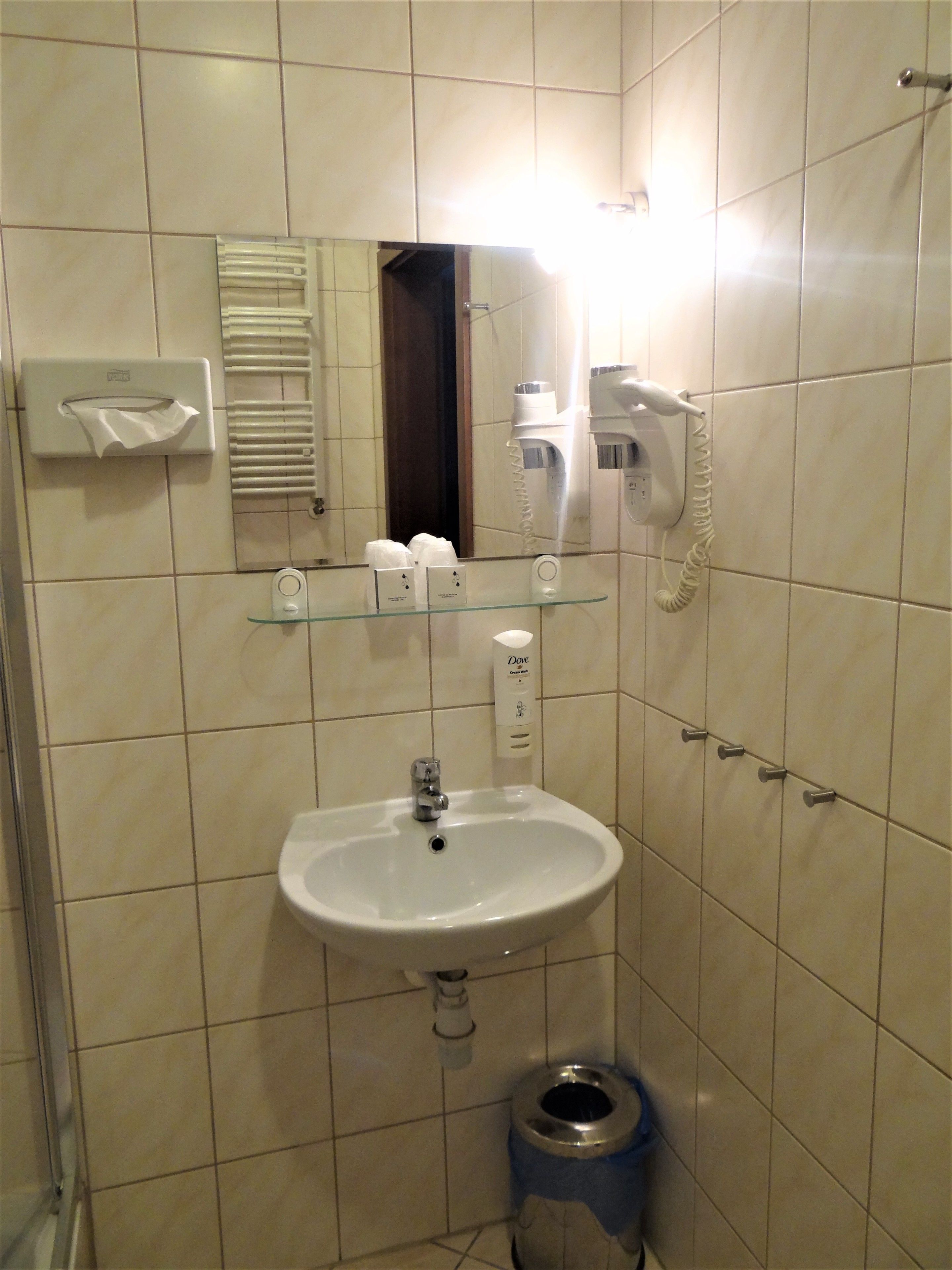 Un baño con lavamanos, espejo, dispensador de toallas y secador de pelo.