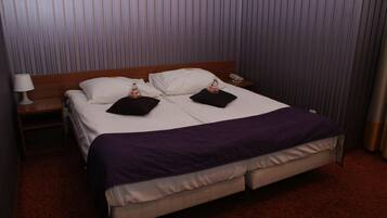 A hotel room with a large bed, two pillows, a bedside table with a lamp, and a telephone.