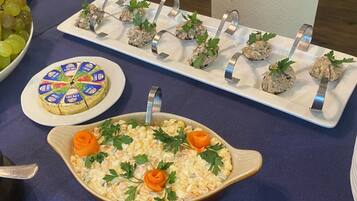 A buffet table with a variety of dishes including a large pot of potato salad, a platter of meatballs, a cheese wheel, and a bowl of grapes.