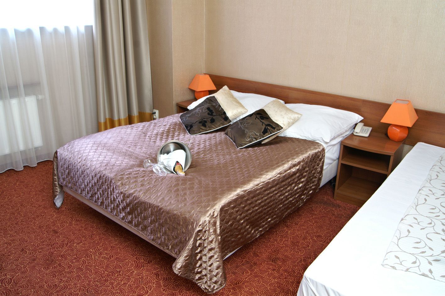 A hotel room with a large bed, two bedside tables, a nightstand, a lamp, and a telephone.