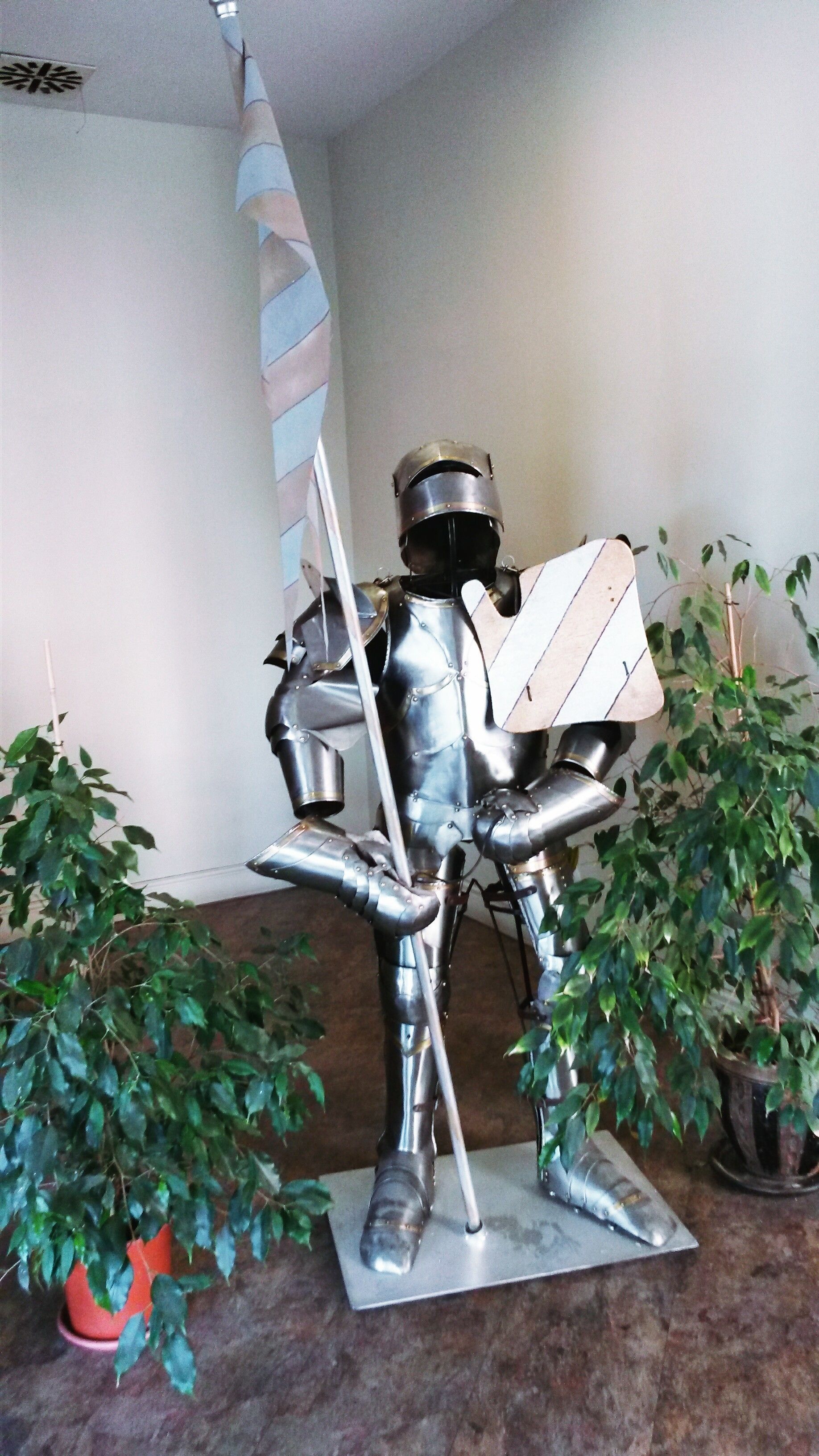 A sculpture of a knight in armor holding a sword and shield, placed on a metal base.