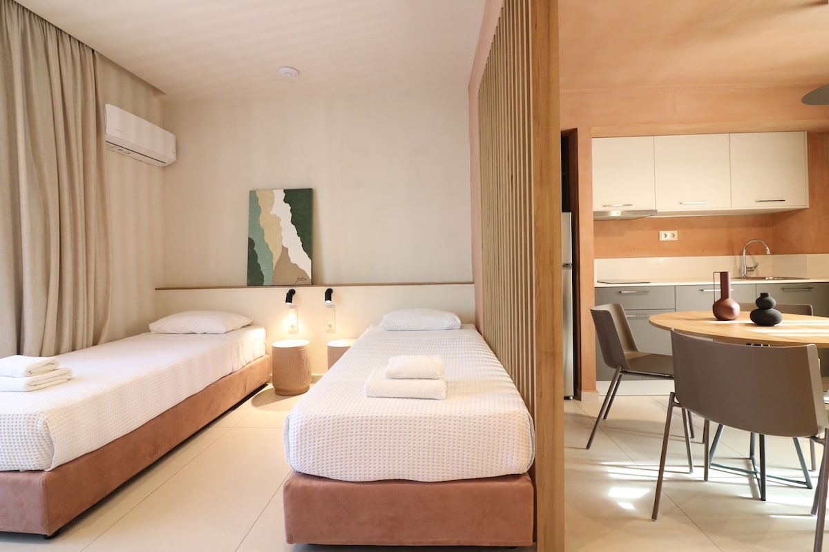 A hotel room with two beds, a dining area, and a kitchenette.