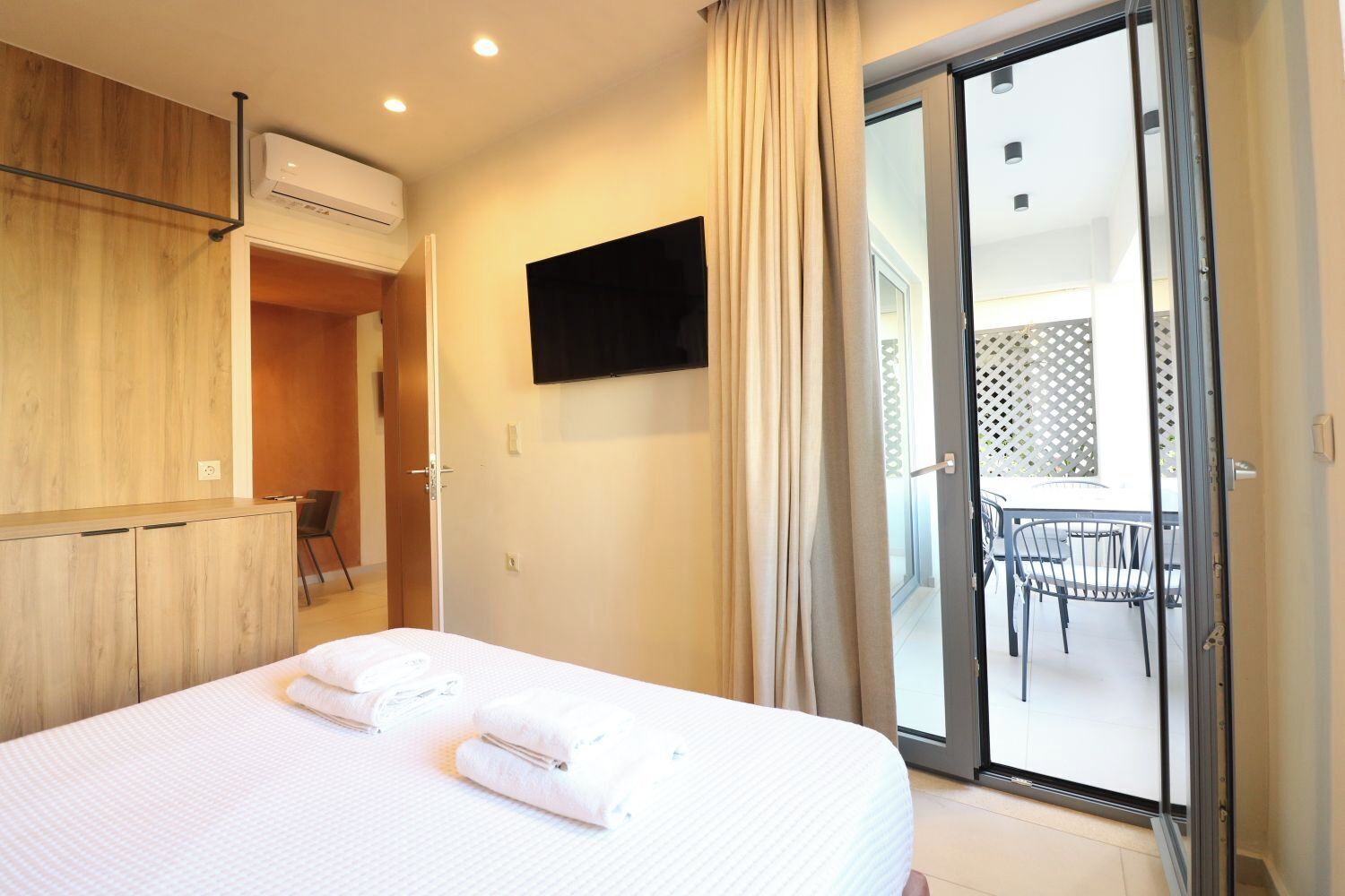 Een hotelkamer met een bed, een aan de muur bevestigde televisie en een schuifdeur naar een buitenruimte met een tafel en stoelen.