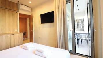 Een hotelkamer met een bed, een aan de muur bevestigde televisie en een schuifdeur naar een buitenruimte met een tafel en stoelen.