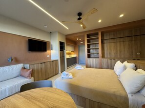 A hotel room with a sofa, two beds, a TV, a ceiling fan, and a kitchenette. - Philoxenia Apartments (Mylopotamos)