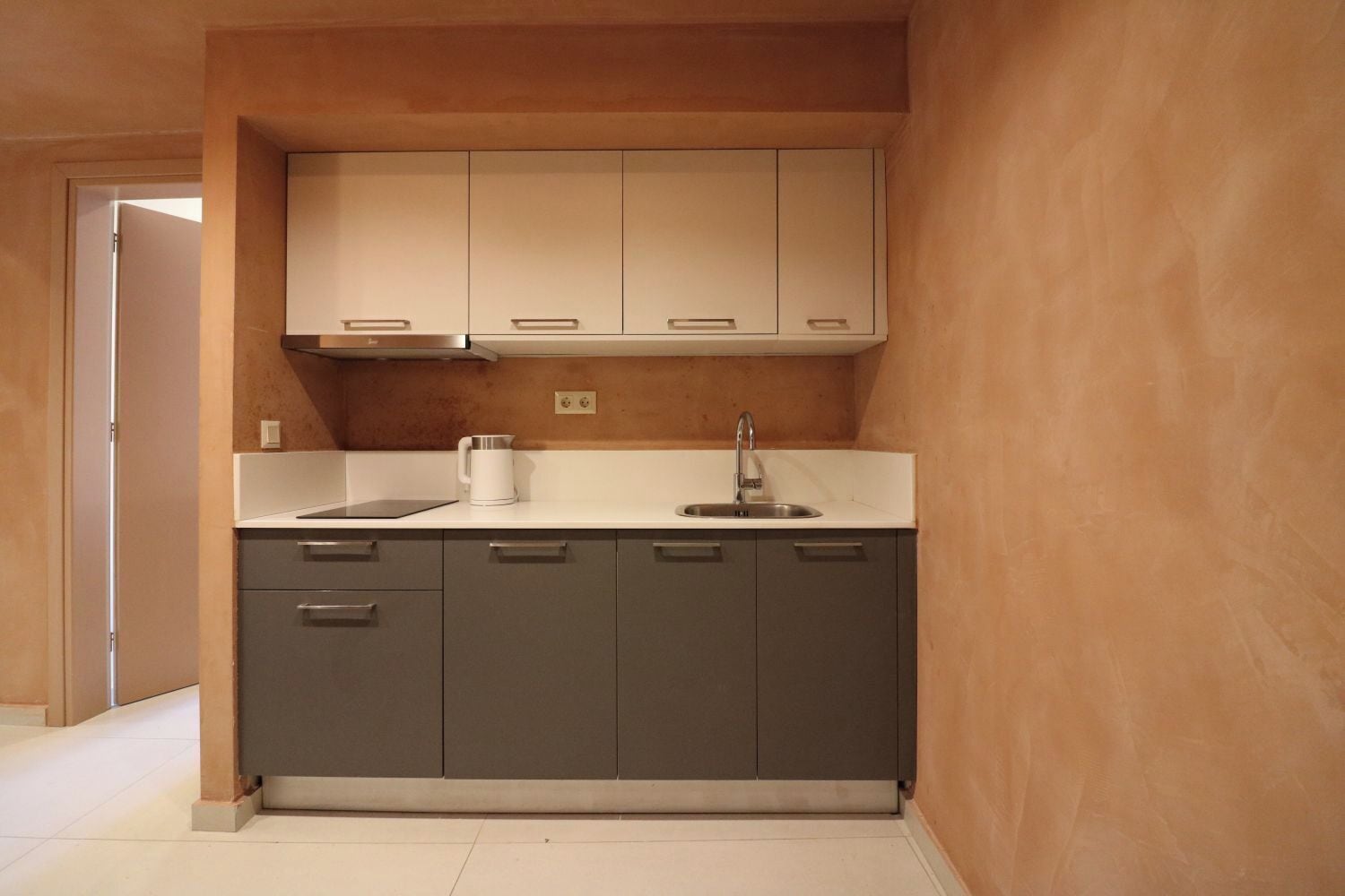 Una cocina compacta con gabinetes grises, una encimera blanca y un lavamanos de acero inoxidable.