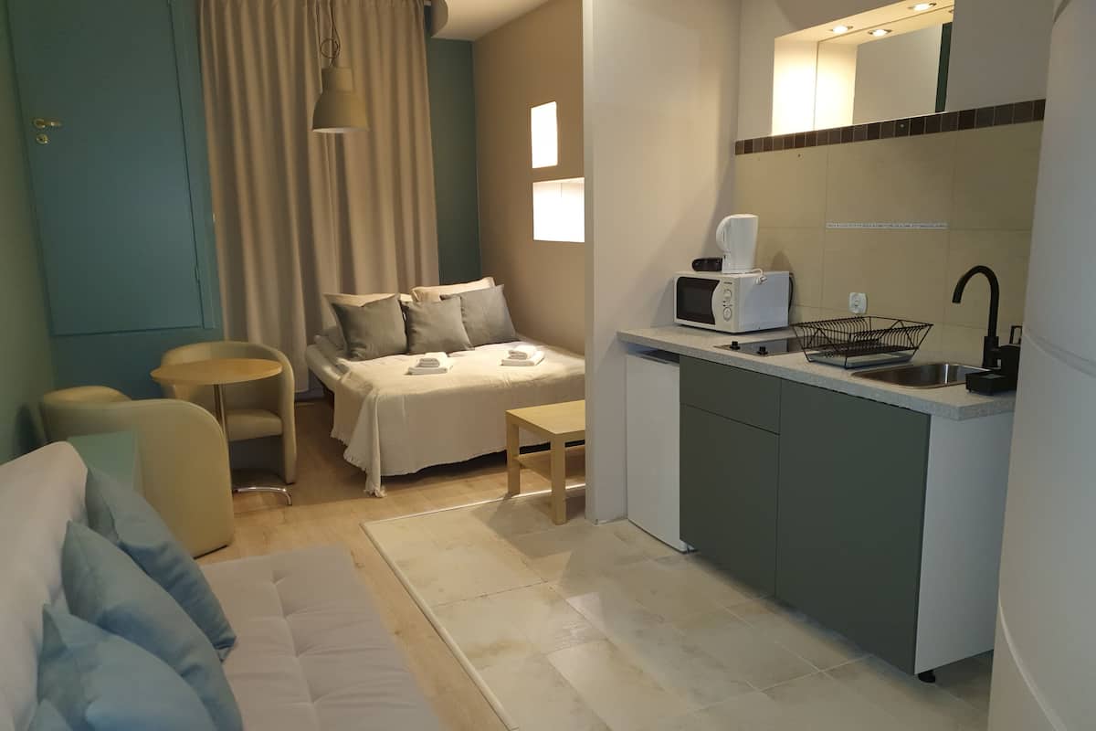 A compact hotel room with a kitchenette, a bed with a white duvet, a small dining table, and a sofa.