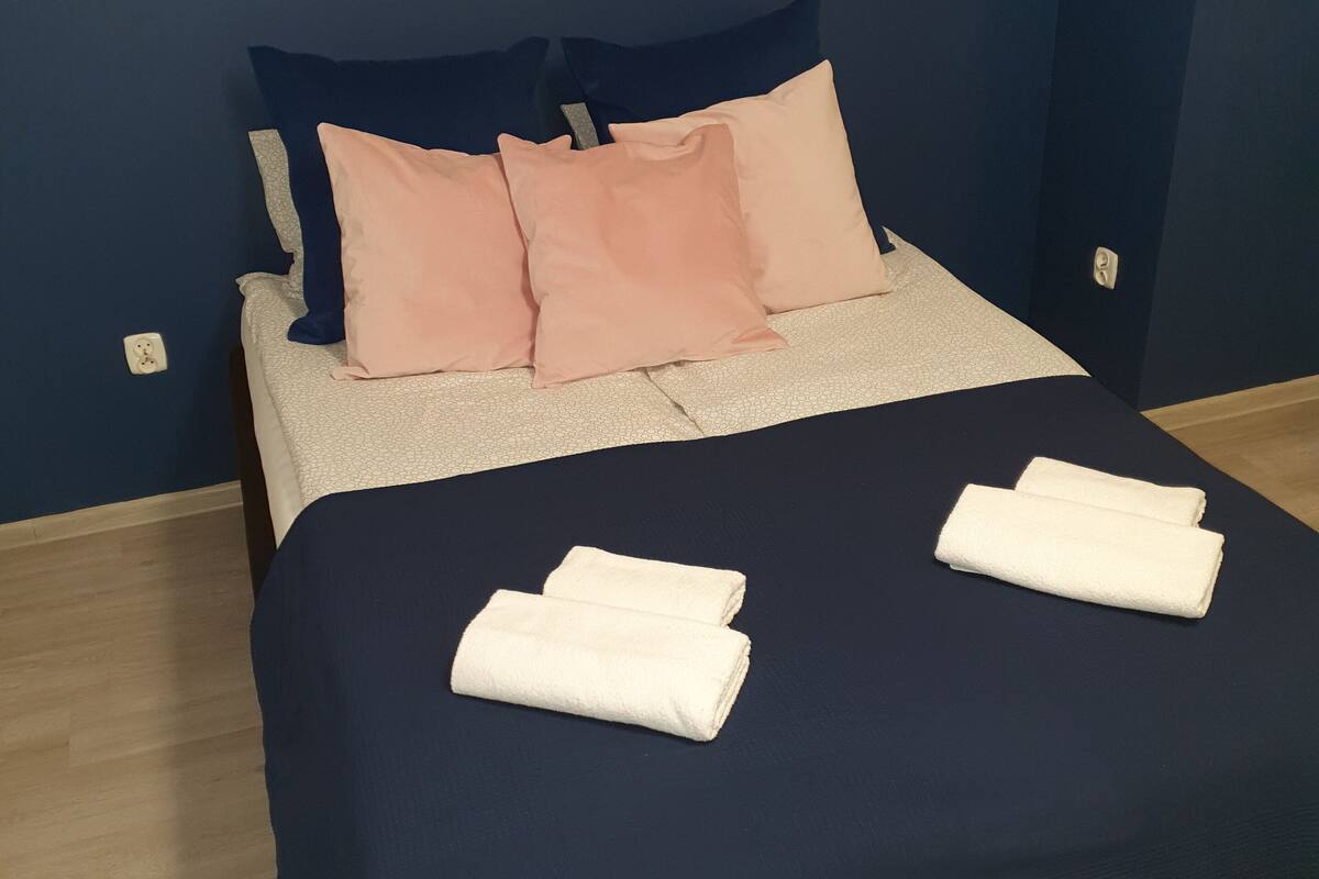 A neatly made bed with a dark blue bedspread and two white towels folded on it.