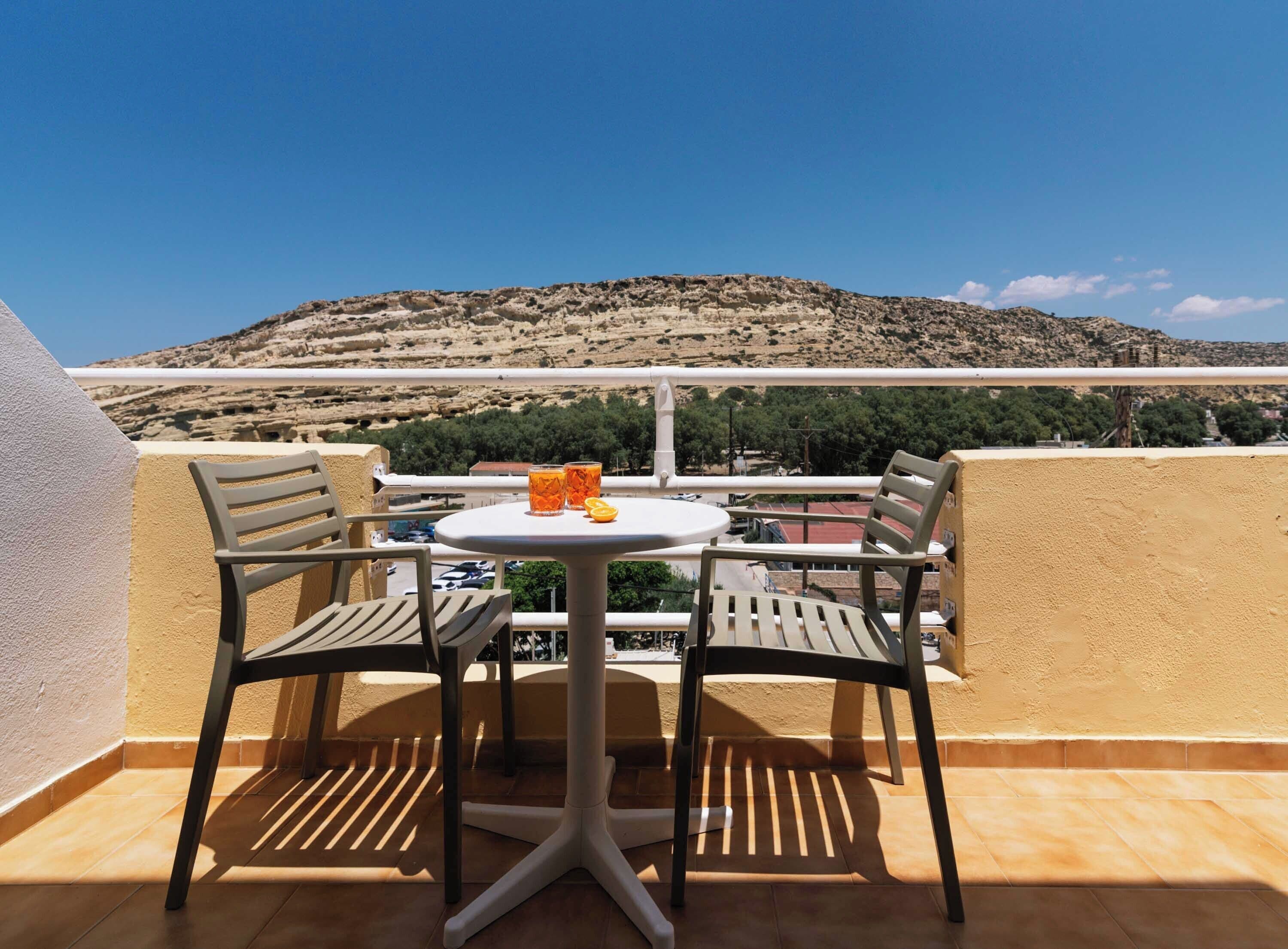 A balcony with two chairs and a table, overlooking a mountainous landscape.