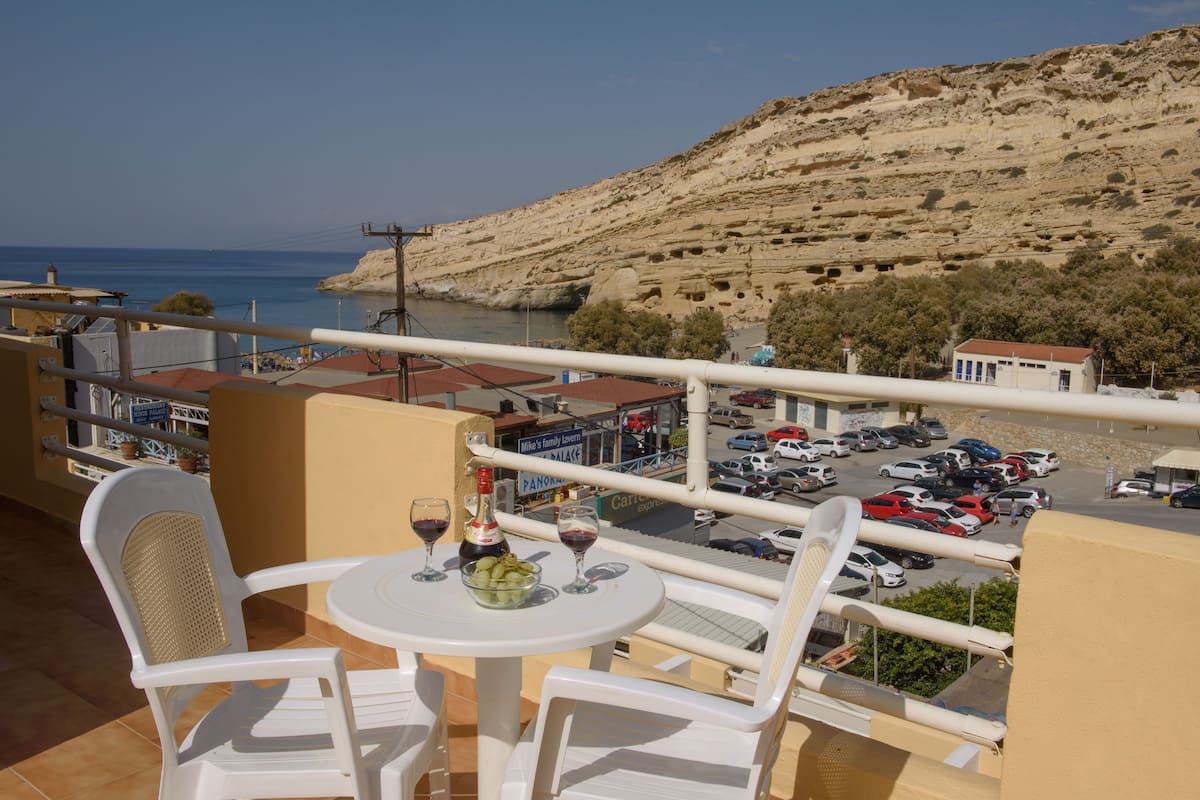 Un balcón con mesa y sillas, con vistas a un estacionamiento y un paisaje montañoso.