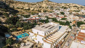 A hotel with a swimming pool, located in a coastal town with a mountainous backdrop.