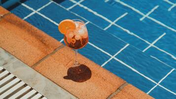 A glass of drink with an orange slice on a poolside with blue tiles and a drain.