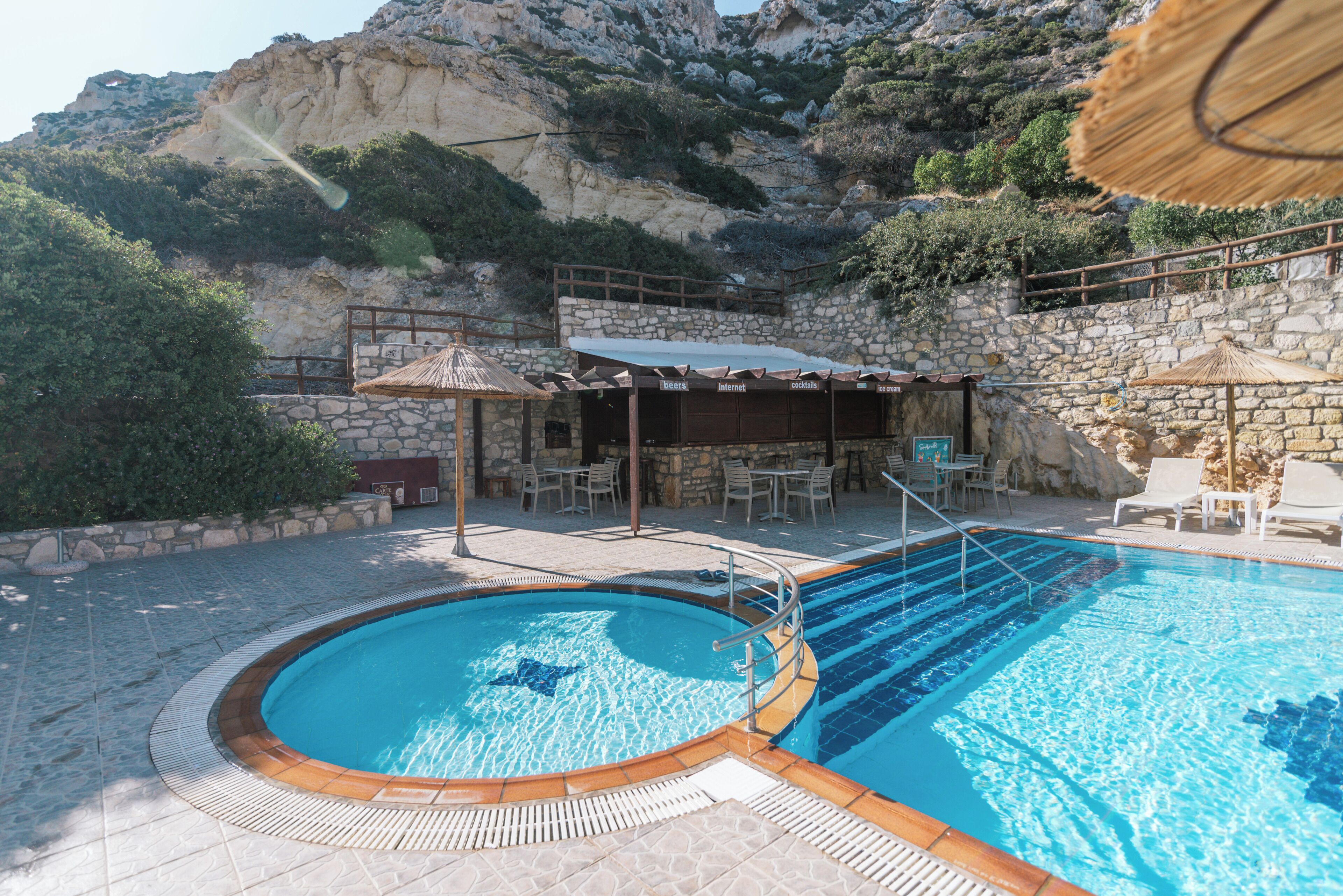 A swimming pool with a stone wall and a covered seating area with umbrellas.