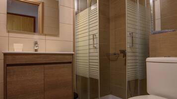 A modern bathroom with a glass-enclosed shower, a wooden vanity, and a white toilet.