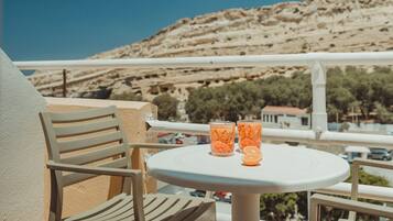 A balcony with a round table and two chairs, two glasses of orange drink, and a view of a mountainous landscape.