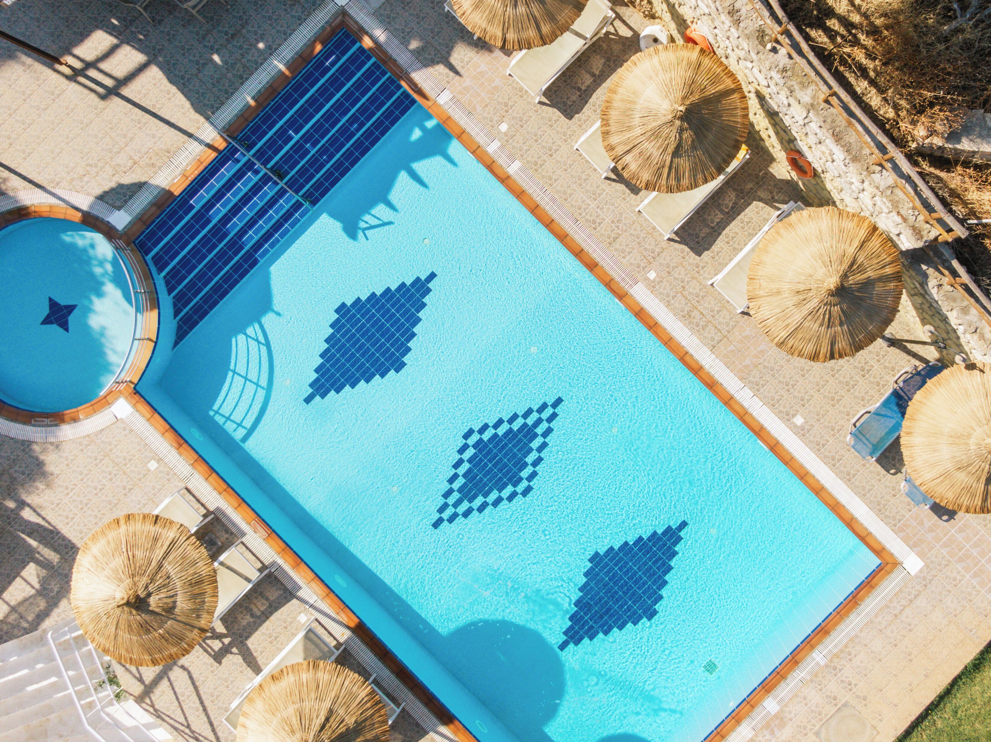 An aerial view of a swimming pool with geometric tile patterns, surrounded by lounge chairs and umbrellas.