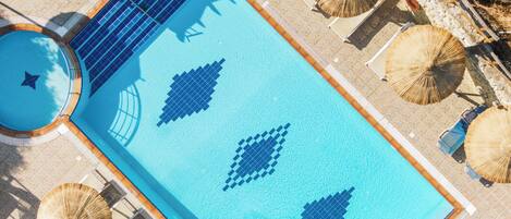 An aerial view of a swimming pool with geometric tile patterns, surrounded by lounge chairs and umbrellas.