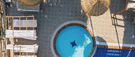 An aerial view of a swimming pool with a star-shaped float, surrounded by lounge chairs and sun umbrellas.