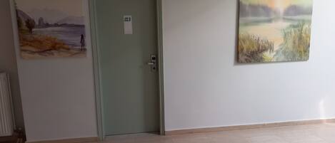 A hallway with a door marked 123, a radiator, and two paintings on the walls.