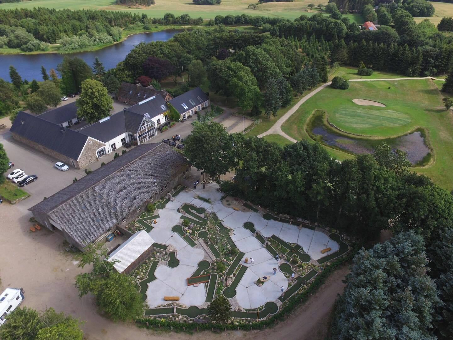 Vue aérienne d’une propriété comprenant un grand bâtiment, un espace de stationnement et un terrain de golf.