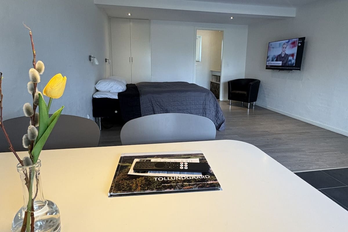 A modern hotel room with a bed, a TV, a desk, and a vase with flowers.