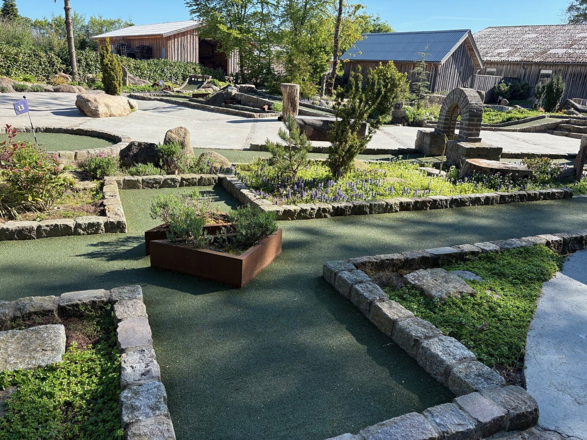 Ein Golfplatz mit Putting Green, Steinrändern und Holzbauten im Hintergrund.