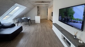 A modern loft apartment with a dining area, a living room with a sofa, a kitchen, and a large TV mounted on the wall. - Tollundgaard Golf Park (Silkeborg)