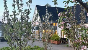 A traditional building with a sloped roof and large windows, surrounded by a garden with flowering trees and shrubs. - Tollundgaard Golf Park (Silkeborg)