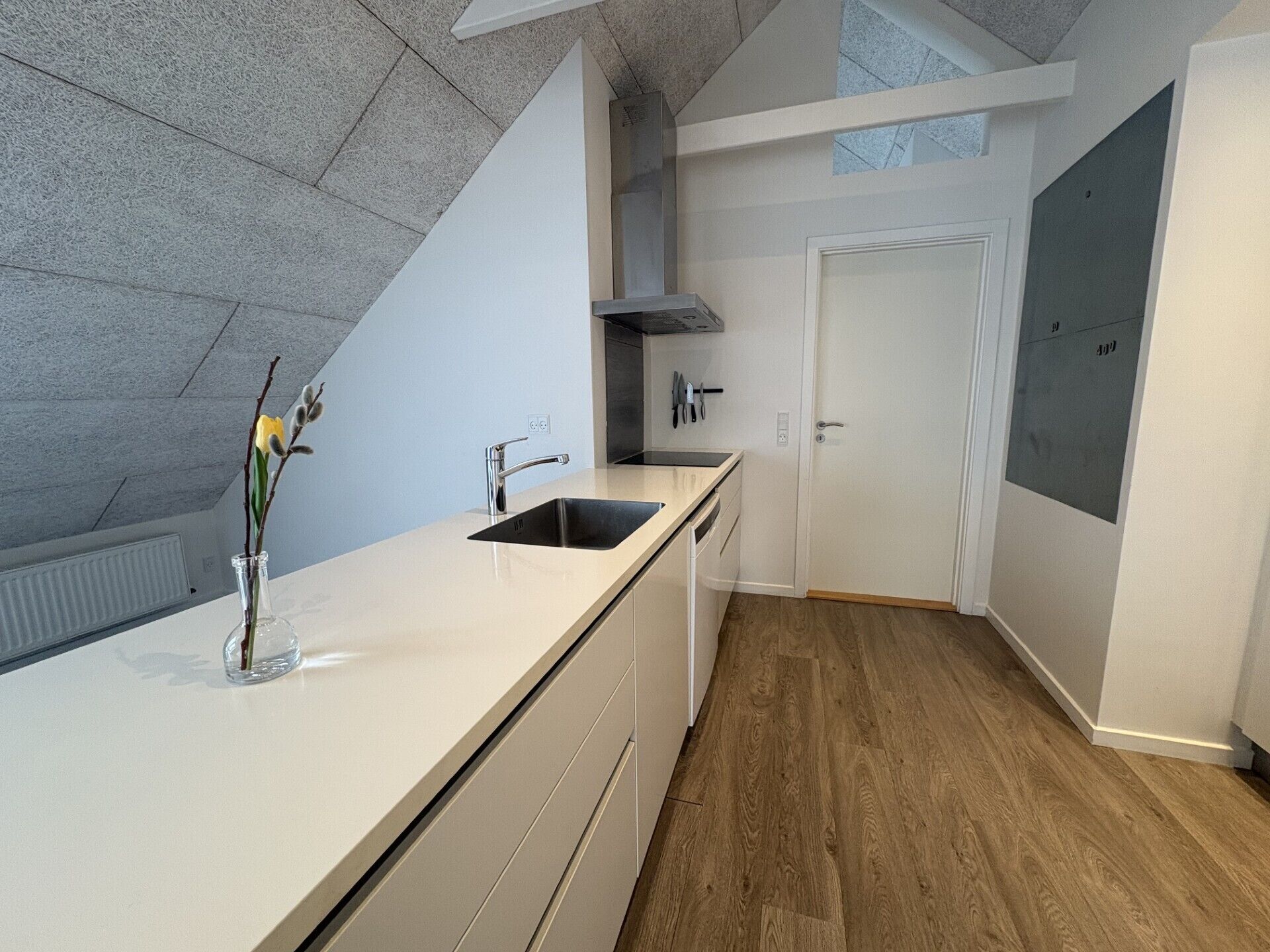 A modern kitchen with a white countertop, stainless steel sink, and a vase with flowers.