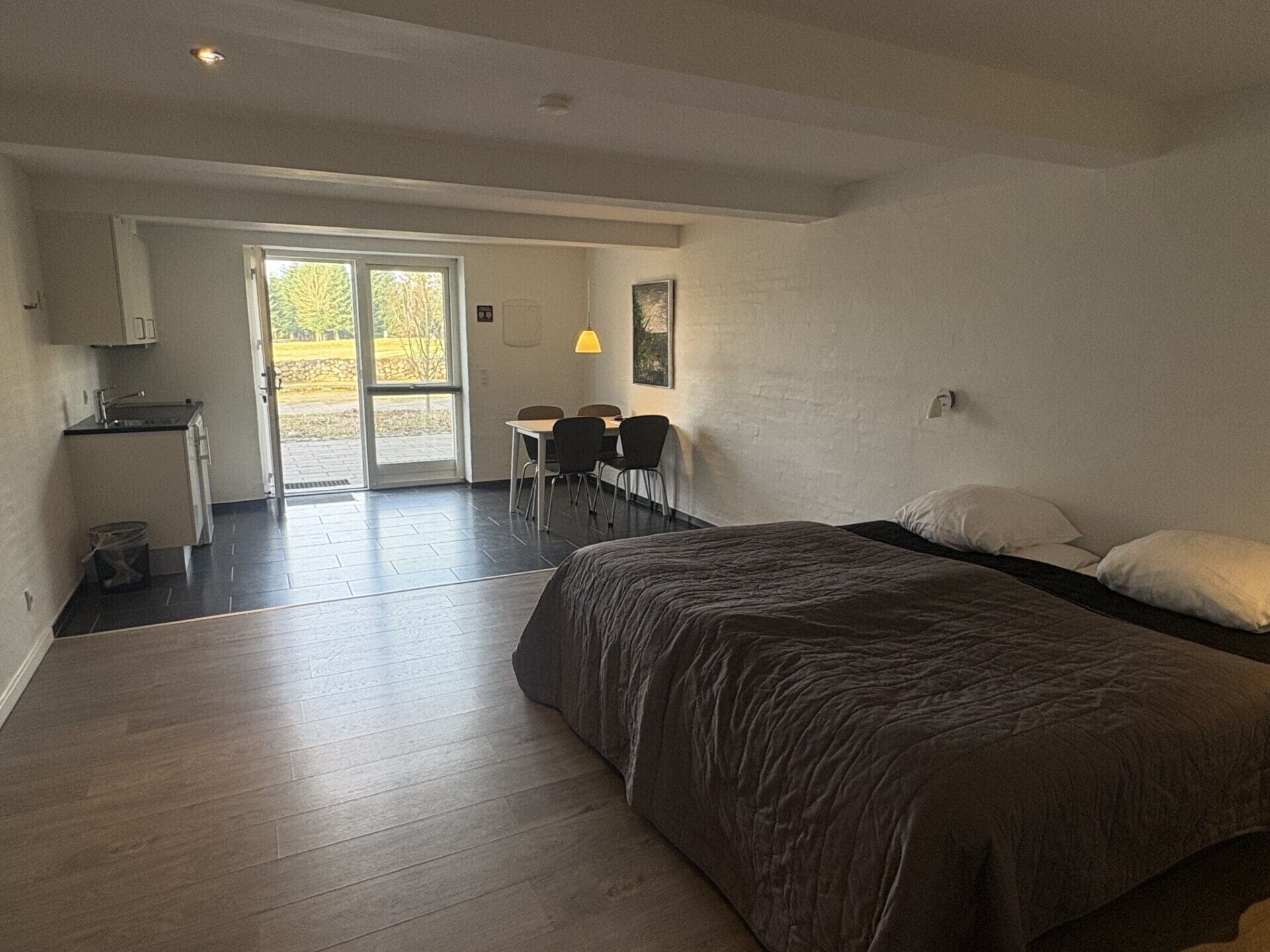 A bedroom with a large bed, a desk, and a chair. There is a door leading to a balcony.