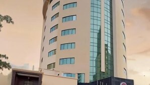 A modern hotel with a curved facade, multiple floors, and a well-maintained garden area with pathways and greenery. - Ramee California Juffair (Manama)