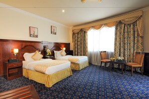 A hotel room with two beds, a wooden headboard, a small table with a vase of flowers, and a chair.