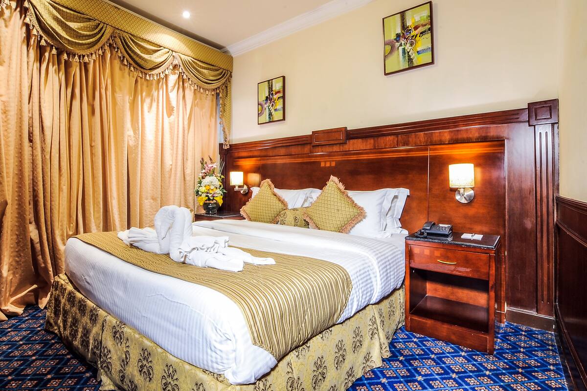 Une chambre d’hôtel avec un grand lit, une tête de lit en bois, une table de chevet avec une lampe et une moquette bleue à motifs.