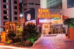 The Ramee California Hotel with a prominent neon sign, a landscaped entrance, and a modern building facade.
