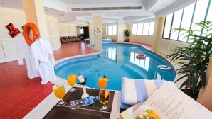 A pool area with a lounge chair, a table with drinks and a menu, and a life ring on a pillar. - Ramee California Juffair (Manama)