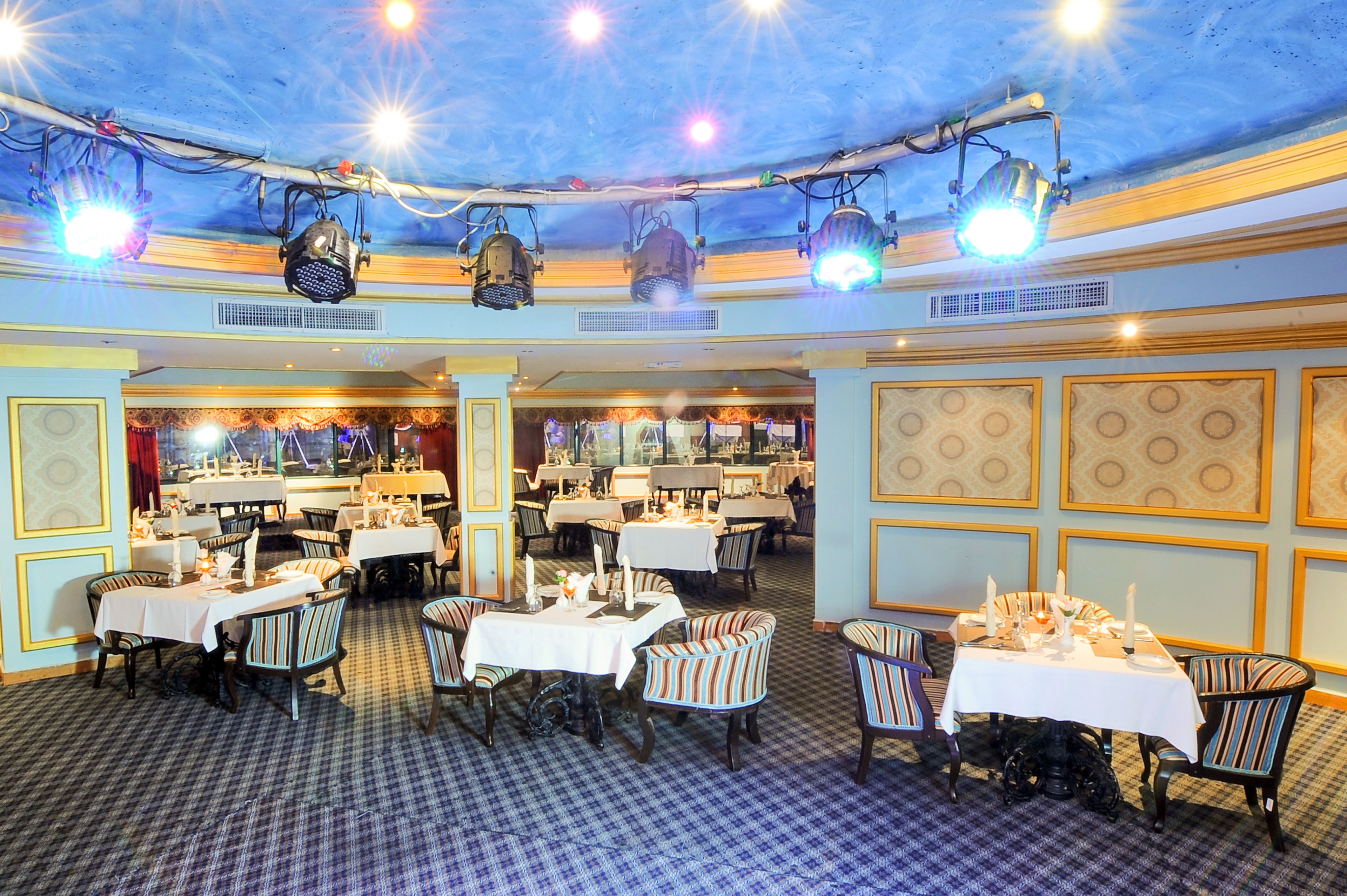 A restaurant with multiple tables and chairs, ceiling lights, and patterned walls.