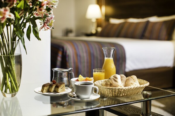 A breakfast table with a vase of flowers, a pitcher, a glass of orange juice, a cup of coffee, and a basket of bread.