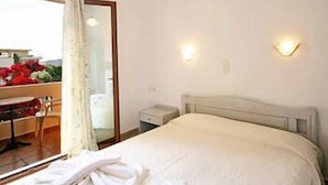 A hotel room with a bed, a nightstand, a mirror, and a window with curtains. - Anniko (Chania)