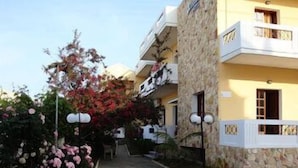A building with a stone facade, a balcony, and a small garden with pink flowers. - Anniko (Chania)